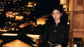 A person standing on a balcony with a view of a traditional building and city lights in the background.