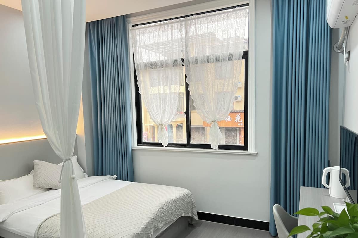 Habitación de hotel con cama, mesita de noche, una silla, ventana con cortinas y vista al exterior.