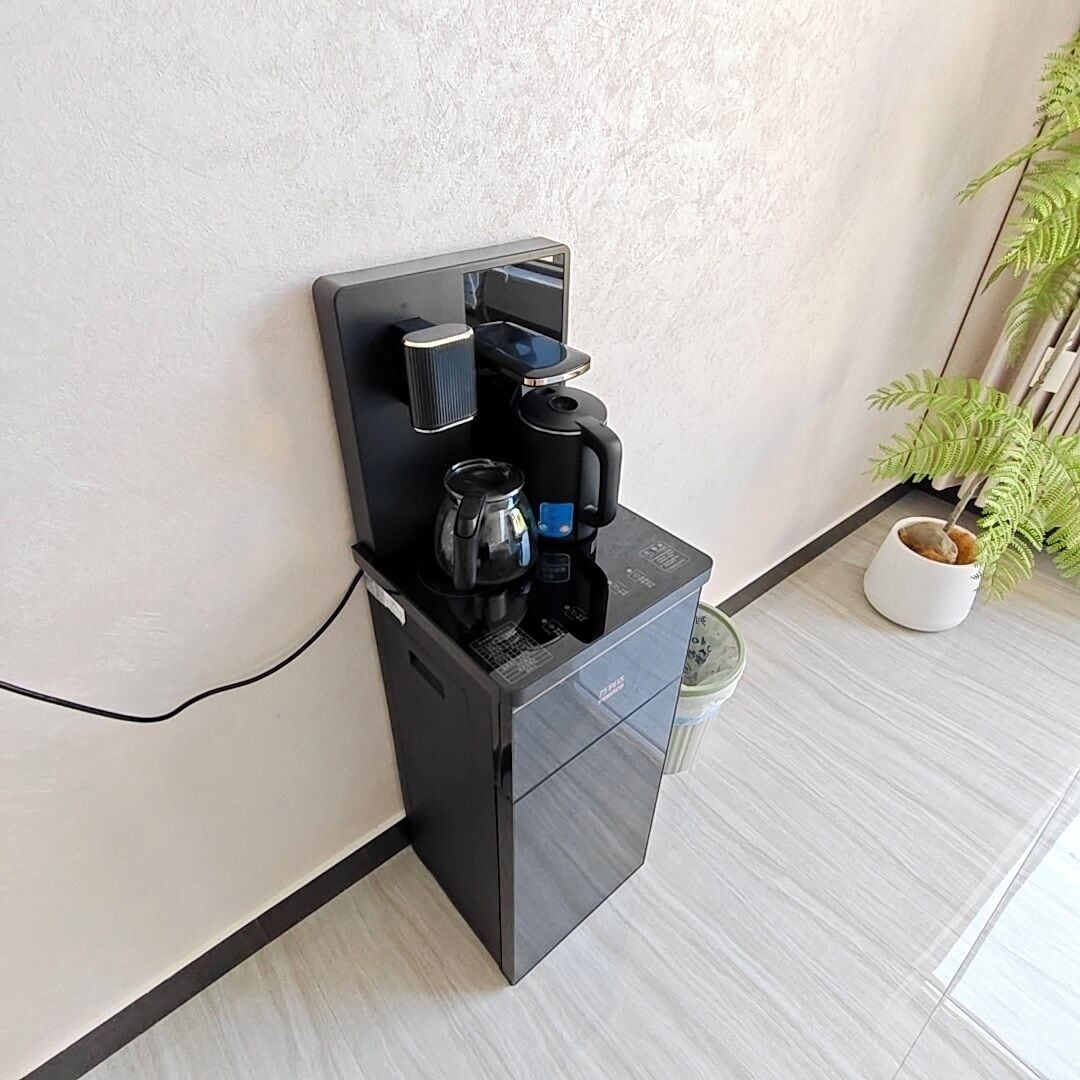 A coffee machine with a kettle and coffee pot, a small potted plant, and a white wall.