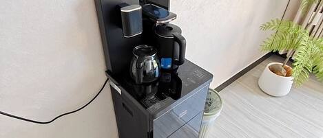 A coffee machine with a kettle and coffee pot, a small potted plant, and a white wall.