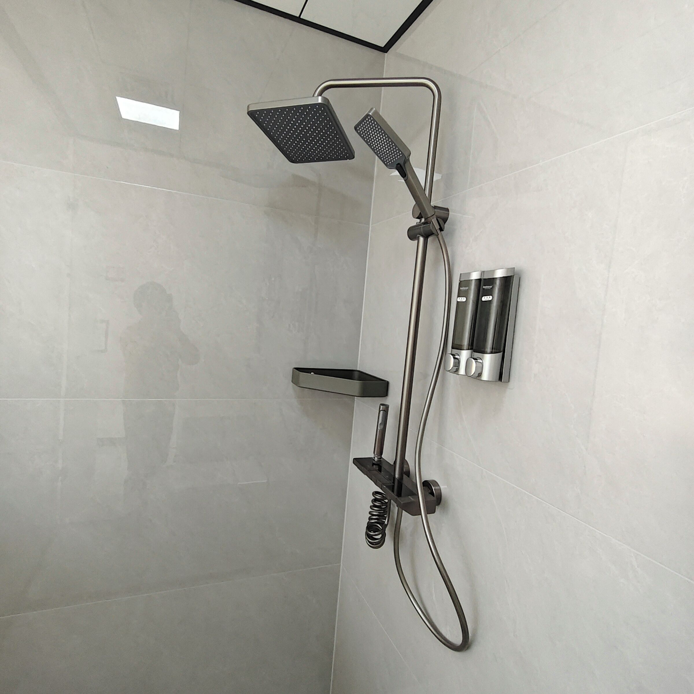A modern shower with a handheld showerhead, a handheld scrubber, and a wall-mounted control panel.