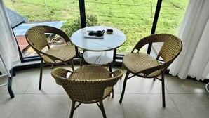 A room with a large window, wicker chairs, a small table with a tray, and a view of green fields and mountains. - Wangxian Valley Qingchuanxingguan - Wangxian Valley Scenic Area  (Shangrao)