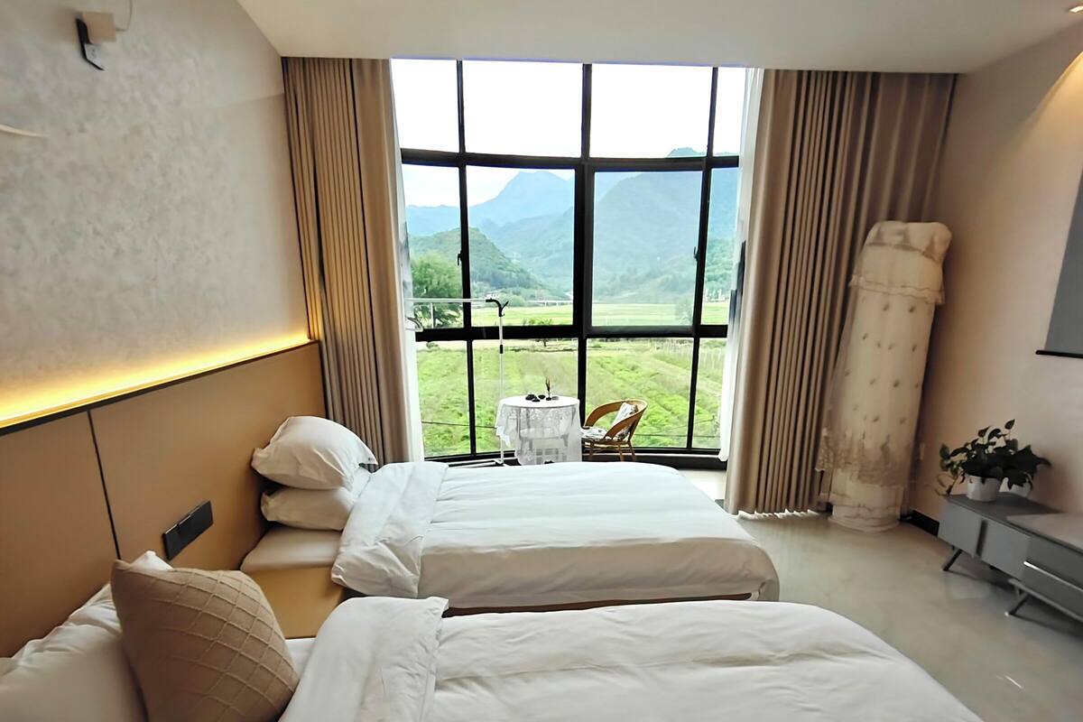 Habitación de hotel con dos camas, vista al campo y un ventanal grande.