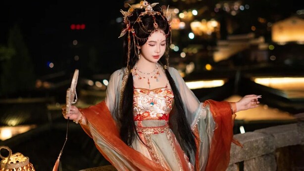 A person in traditional attire standing on a stone structure with a cityscape in the background.