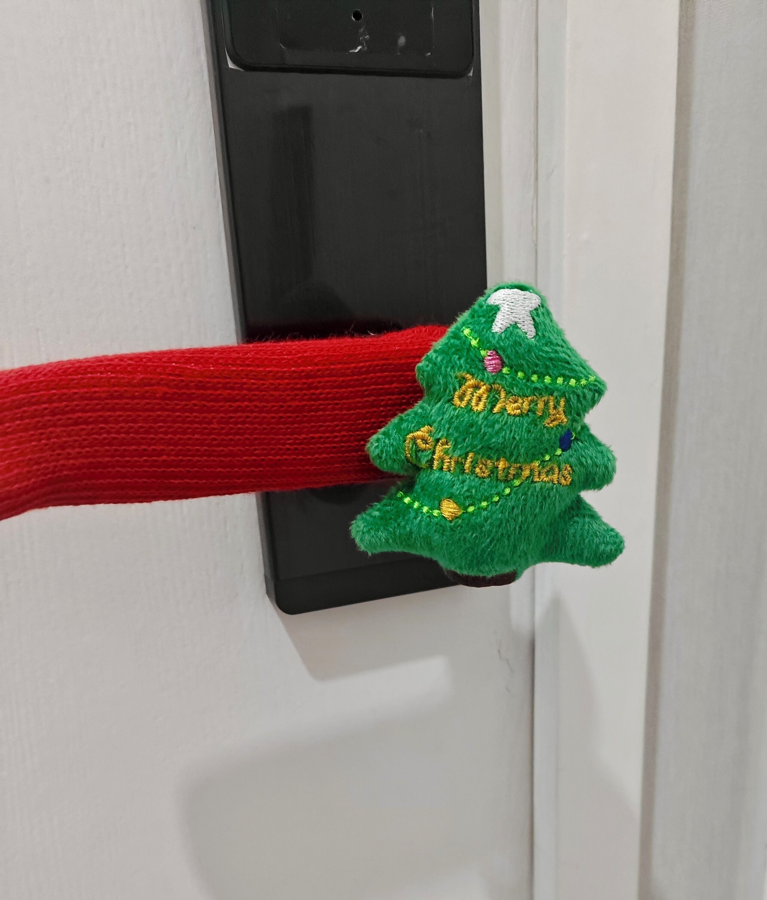 Un picaporte con una cuerda roja y un adorno navideño verde que dice "Merry Christmas".