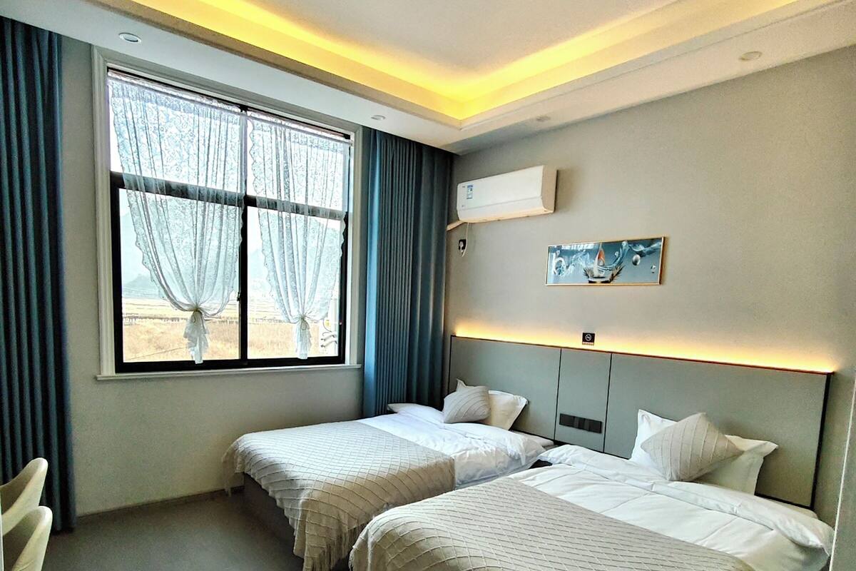 Habitación de hotel con dos camas, una ventana con cortinas, aire acondicionado y una obra de arte colgada en la pared.