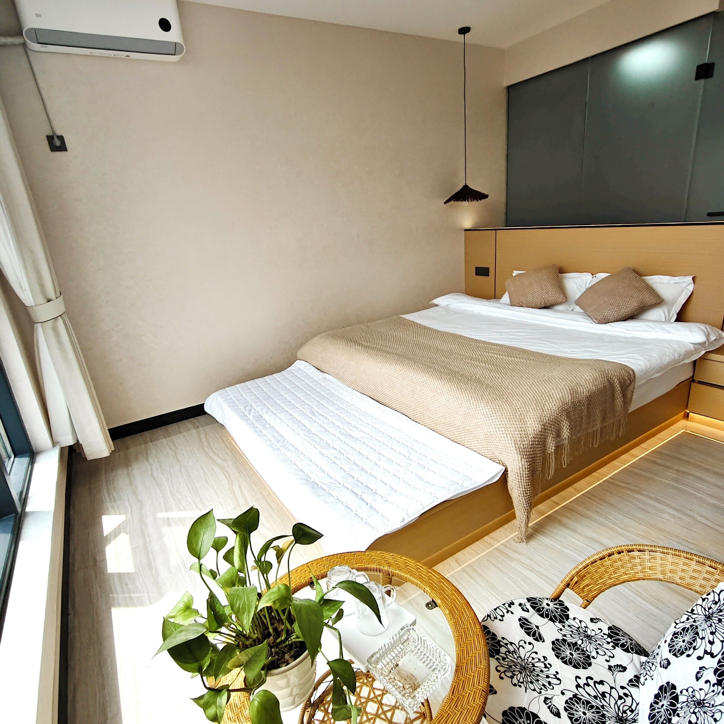 A hotel room with a bed, a bedside table with a plant, a lamp, and a large window.