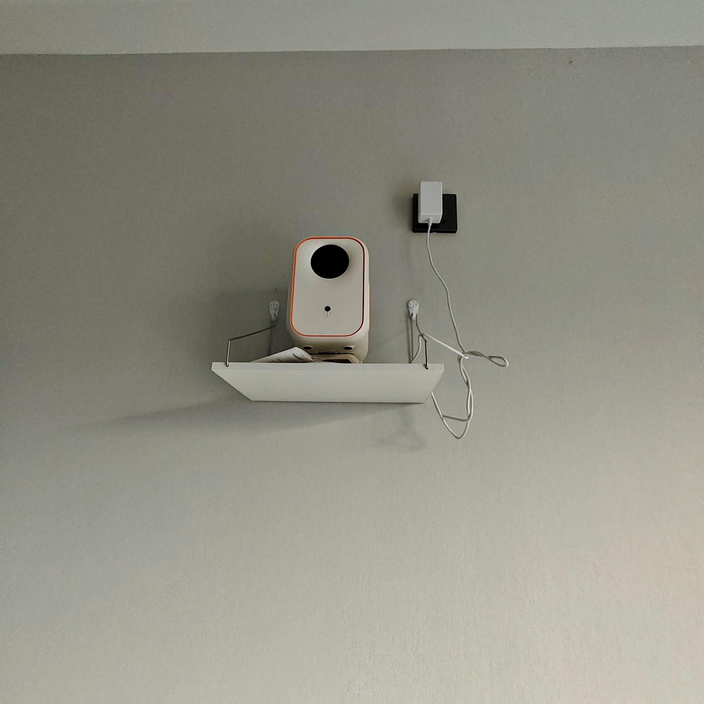 A white shelf with a white speaker on it, mounted on a plain wall.