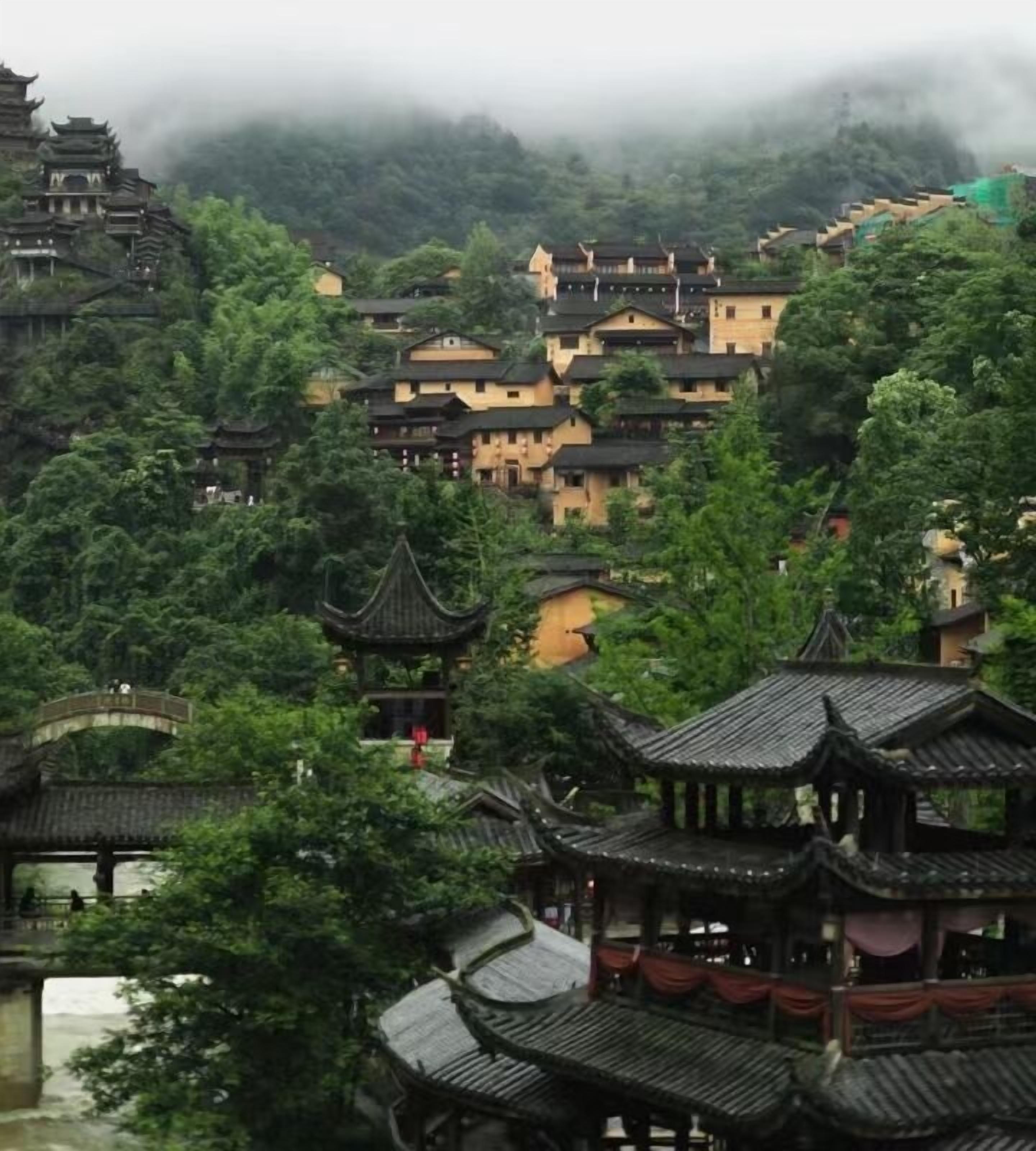 A traditional Chinese village with tiered buildings and pagoda-style structures amidst lush greenery.