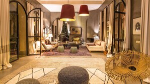 Een ruime woonkamer met een grote bank, fauteuils, een salontafel en een bijzondere rieten stoel. Twee grote hanglampen zijn aan het plafond bevestigd.