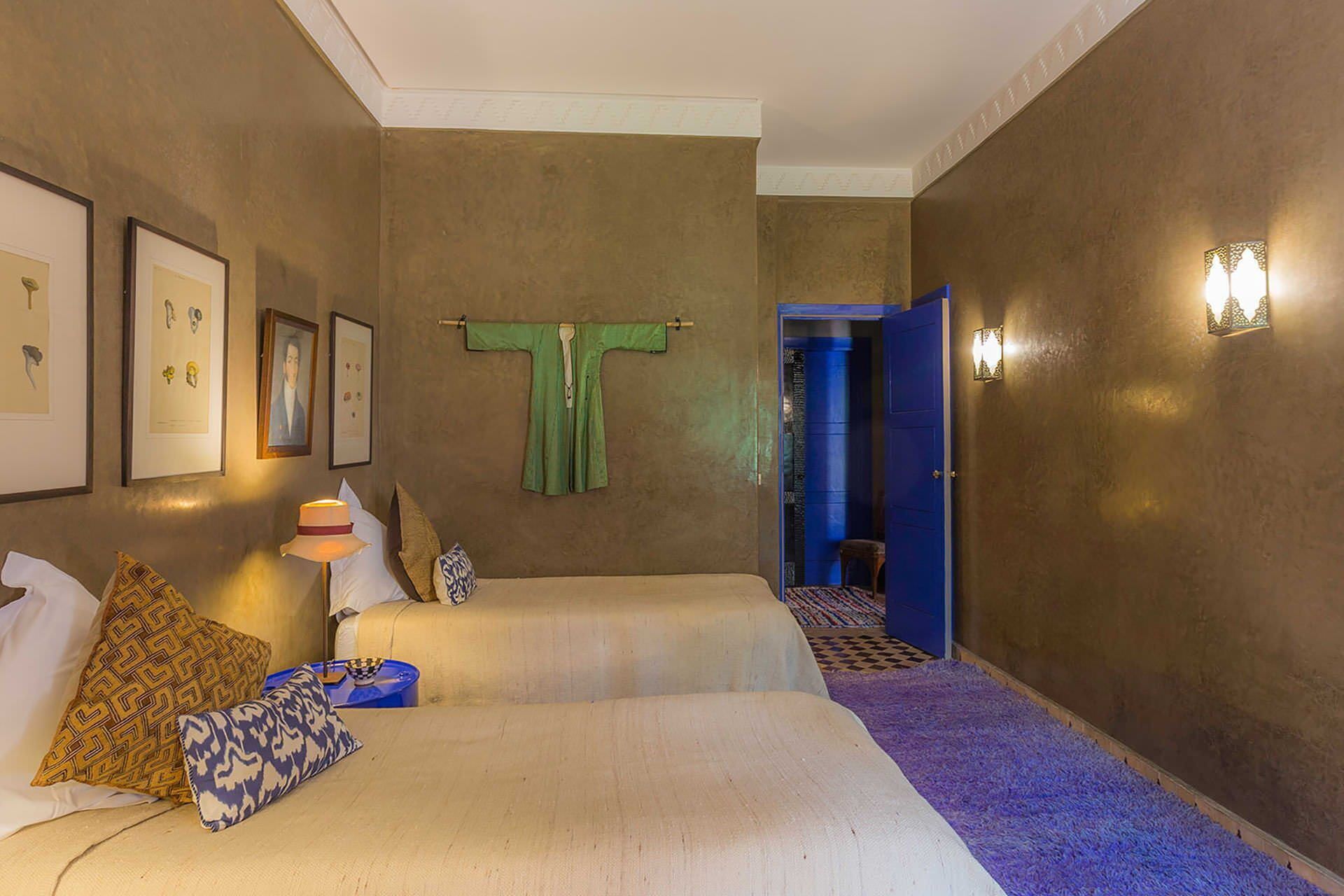 Een hotelkamer met twee bedden, een groene handdoek die hangt, ingelijste foto's aan de muur en een blauwe deur op de achtergrond.