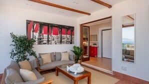 A living room with a sofa, a coffee table, and a large painting. There is a door leading to a balcony with a view of the sea. - Casa Mario with terrace and sea view (Sorrento)