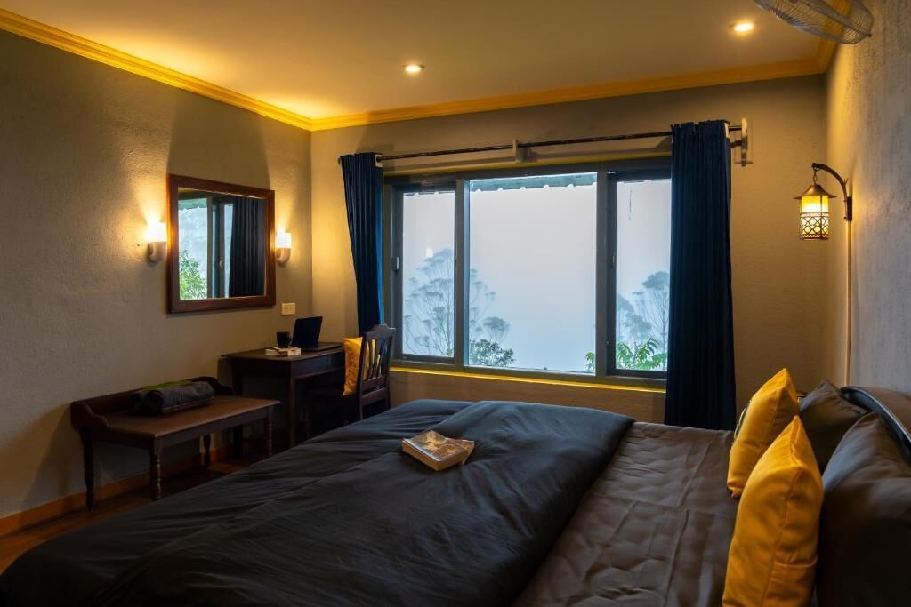 A bedroom with a large bed, a desk, a chair, and a window with curtains.