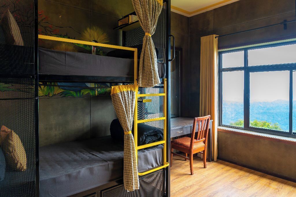 Una cama litera con cortina a cuadros, una silla y un ventanal con vistas.