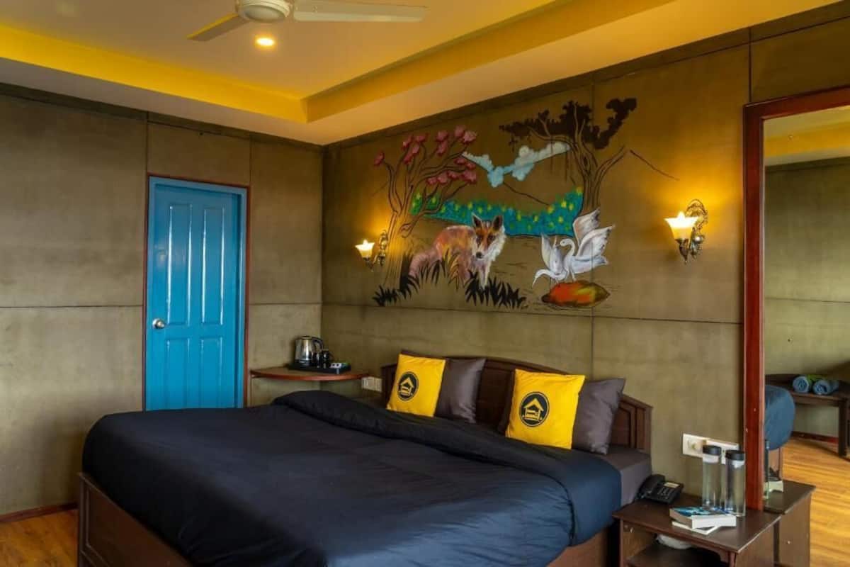 A bedroom with a bed, a blue door, a wall mural, and a nightstand with a lamp.