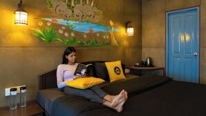 Iemand leest een boek in een kamer met een muurschildering van olifanten en een rivier, een blauwe deur en twee wandlampen.