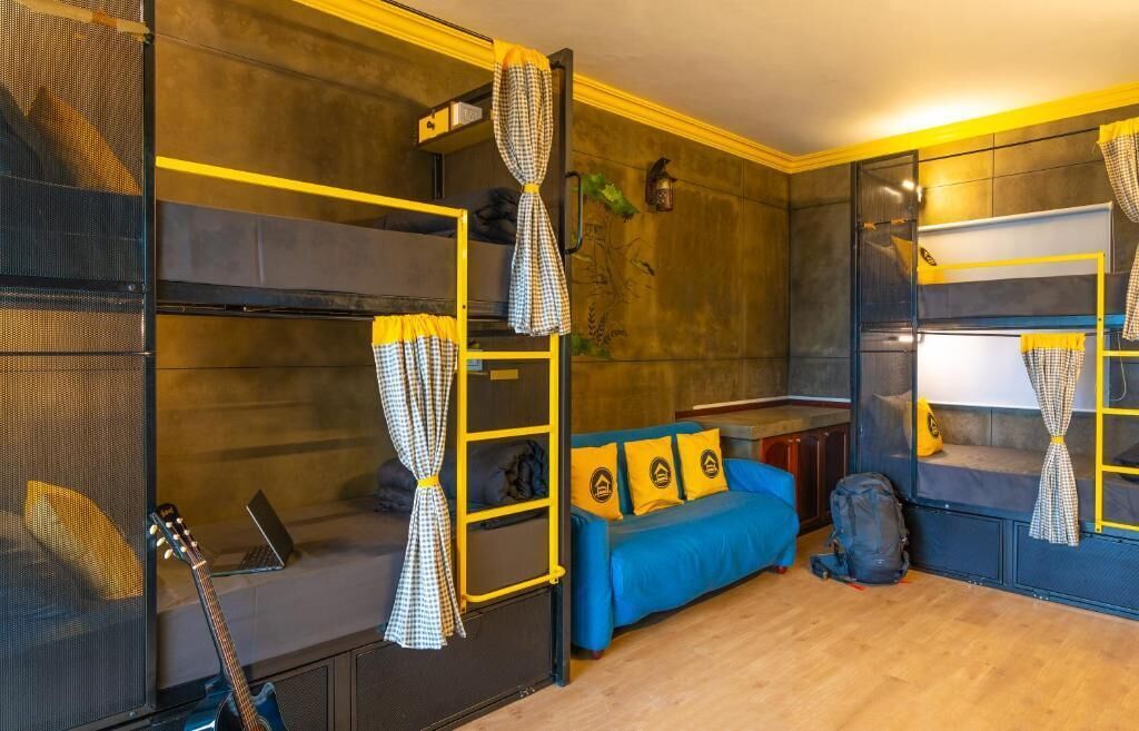 Habitación con literas, un sofá azul, almohadas amarillas y una guitarra.