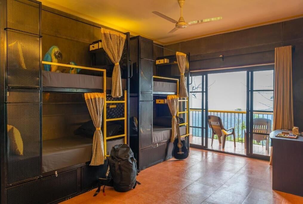 Una habitación con literas, ventilador de techo, balcón con una silla y una mesa con objetos encima.