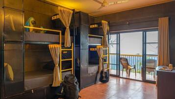 Una habitación con literas, ventilador de techo, balcón con una silla y una mesa con objetos encima.