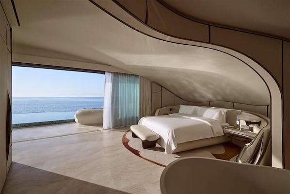 Un dormitorio espacioso con techo curvo, una cama grande, un banco y vistas al mar.