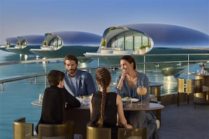 Un grupo de personas cenando en una mesa con vistas a arquitectura futurista y agua.