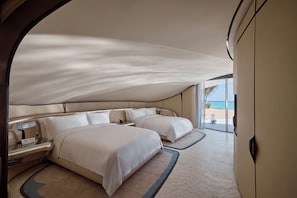 Habitación de hotel moderna con dos camas grandes, una mesita de noche y vista a la playa.
