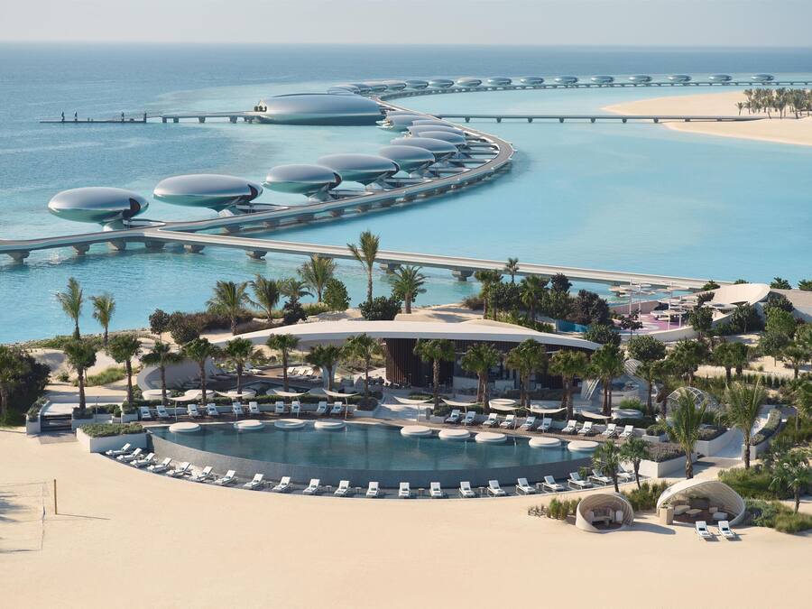 Un resort con una piscina amplia, tumbonas, palmeras y una playa.