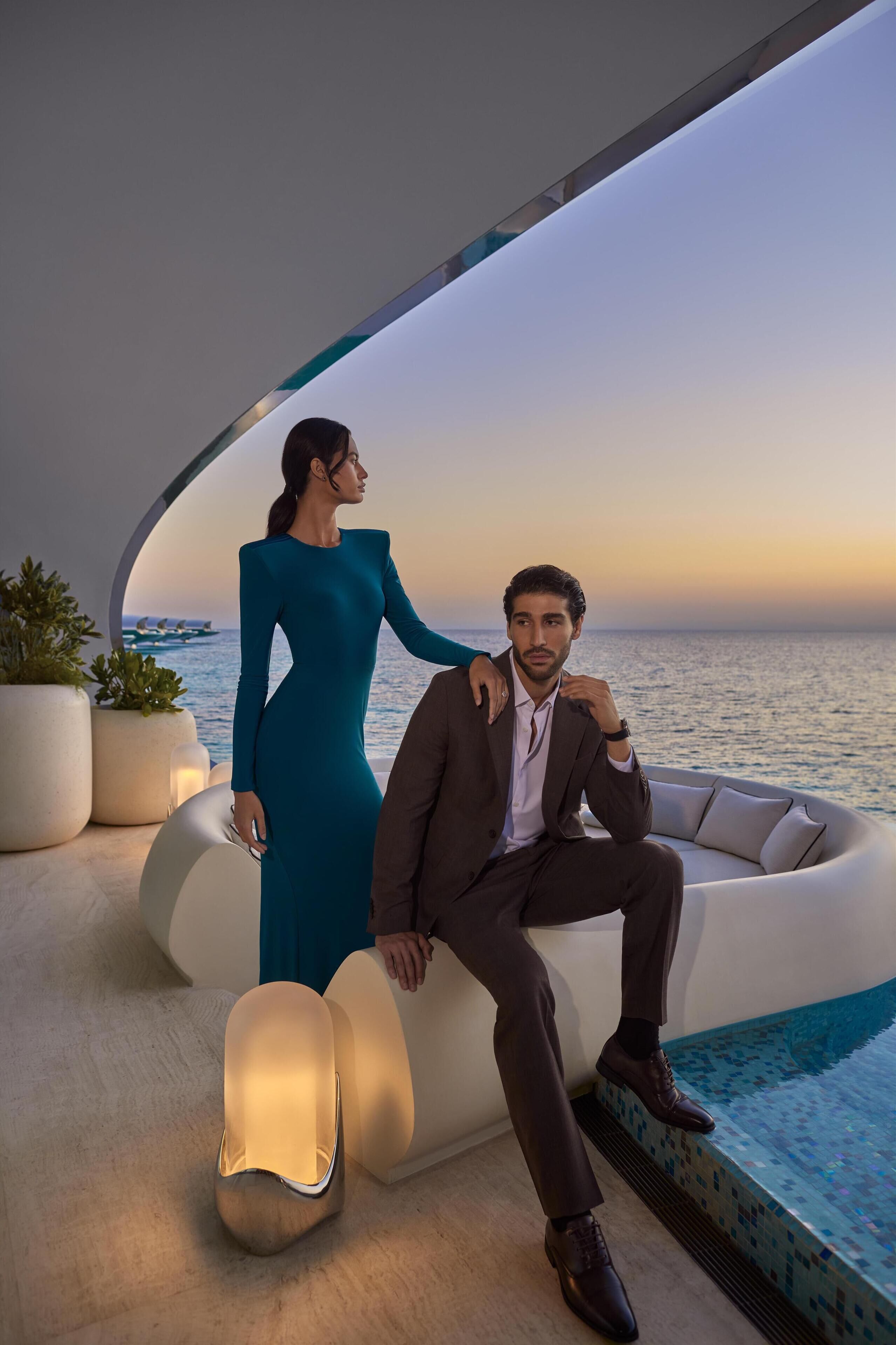 Ein Mann und eine Frau in festlicher Kleidung sitzen am Pool mit Blick auf das Meer.