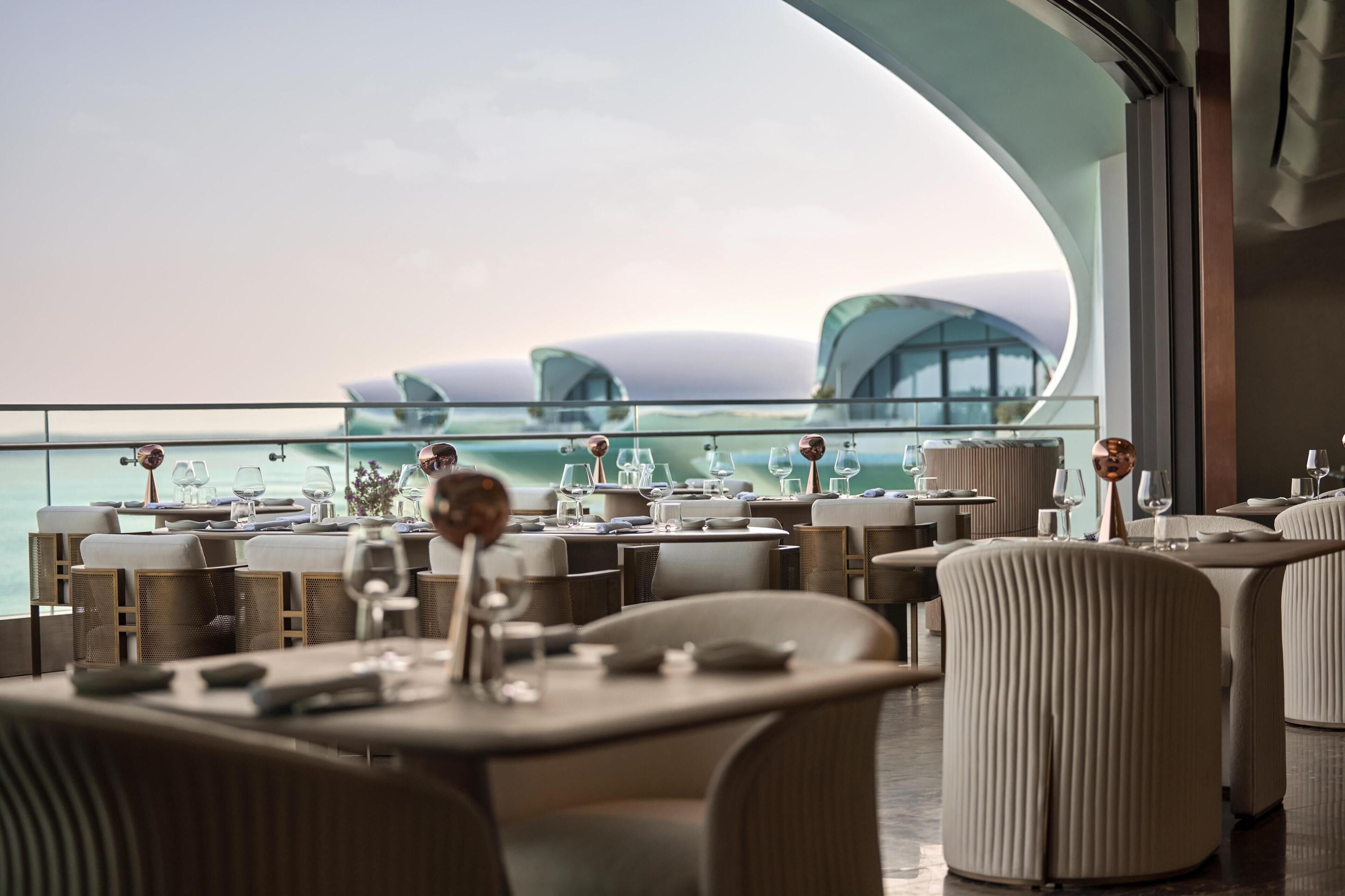 Een modern restaurant met gedekte tafels, met een panoramisch uitzicht op zee.
