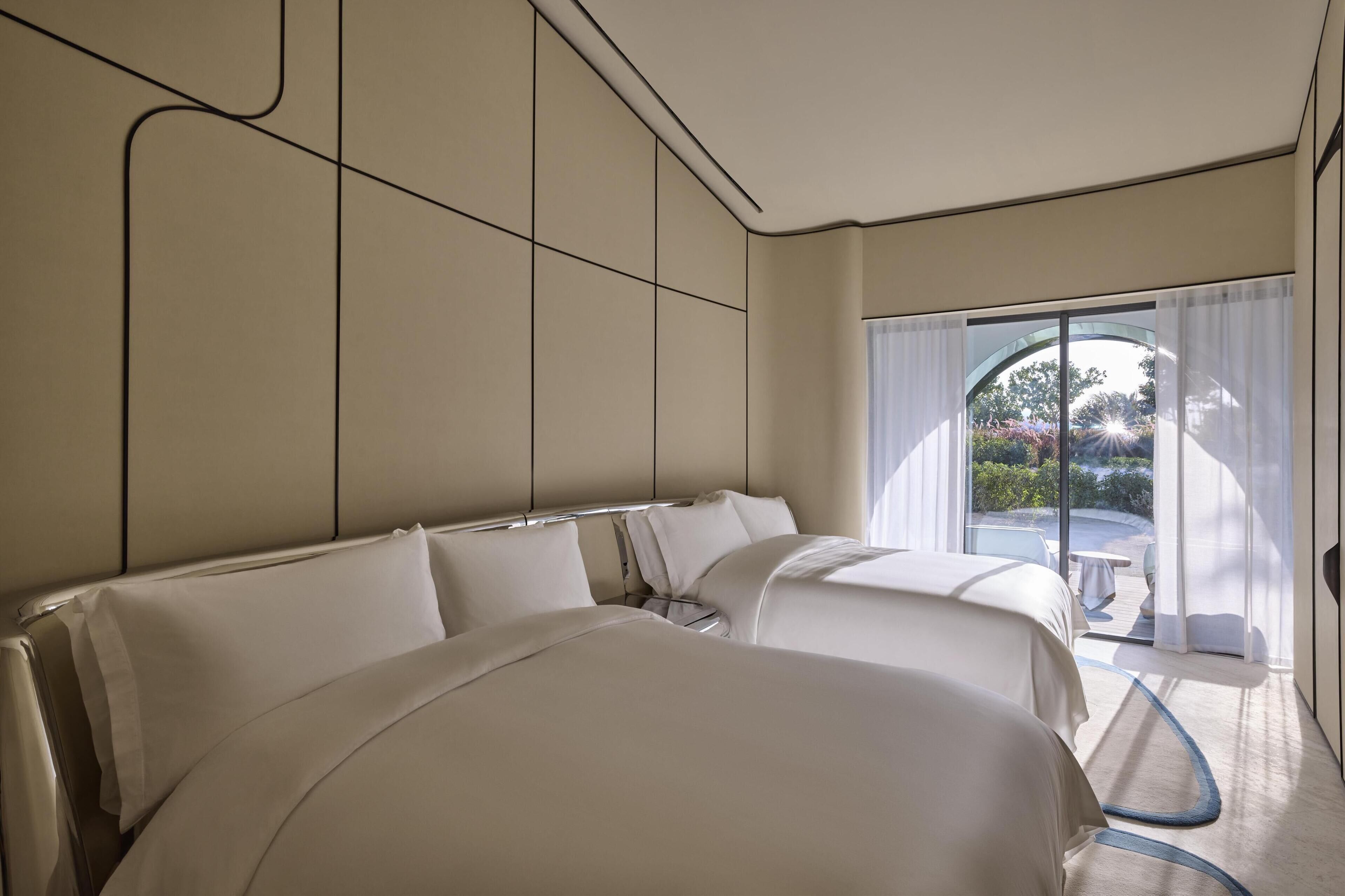 Quarto de hotel moderno com duas camas, uma janela grande com cortinas e vista para o exterior.