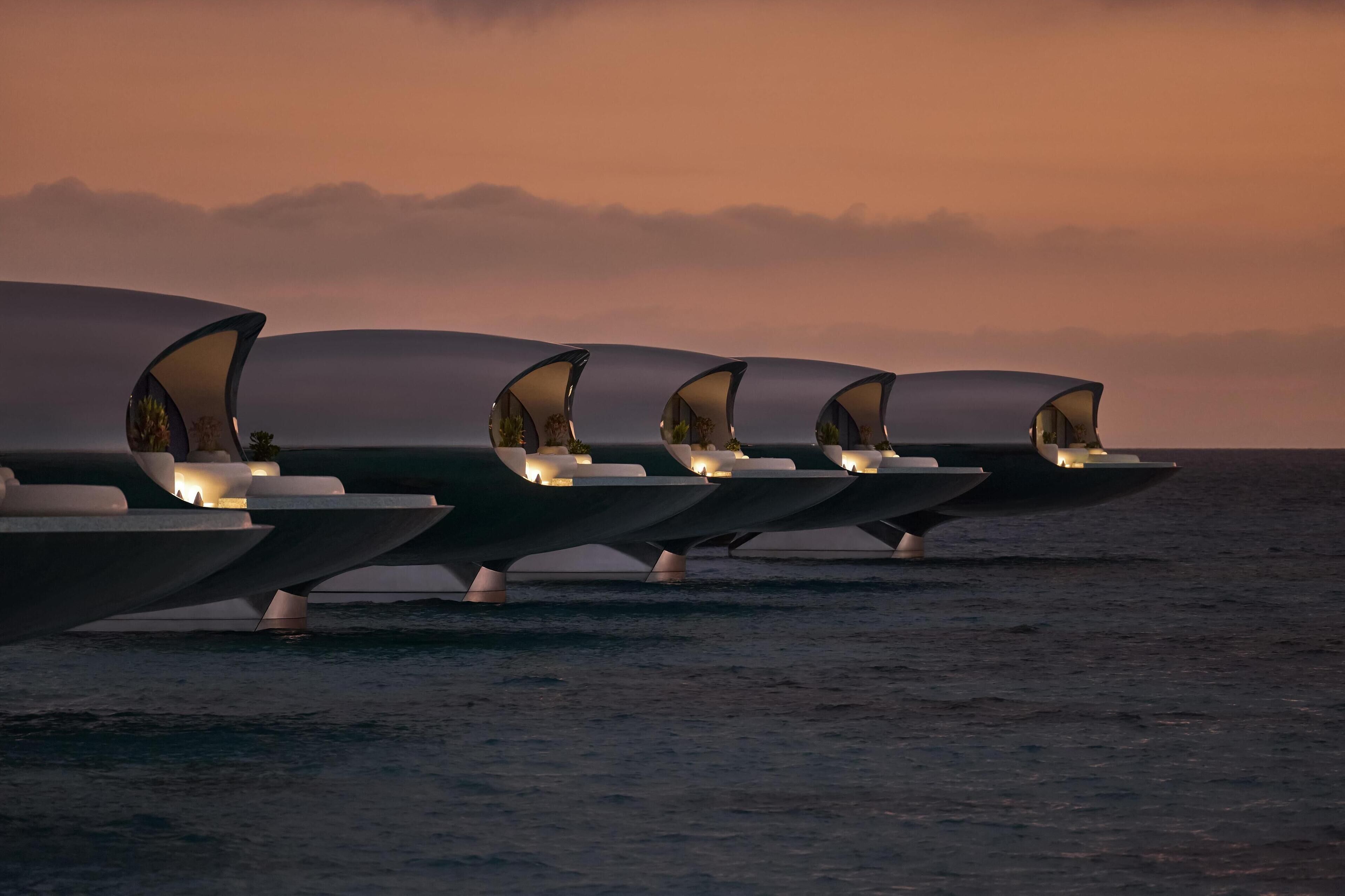 Une rangée de structures modernes et élégantes, aux formes évoquant des bateaux et aux côtés ouverts, qui semblent servir d’hébergement original ou d’espace événementiel.