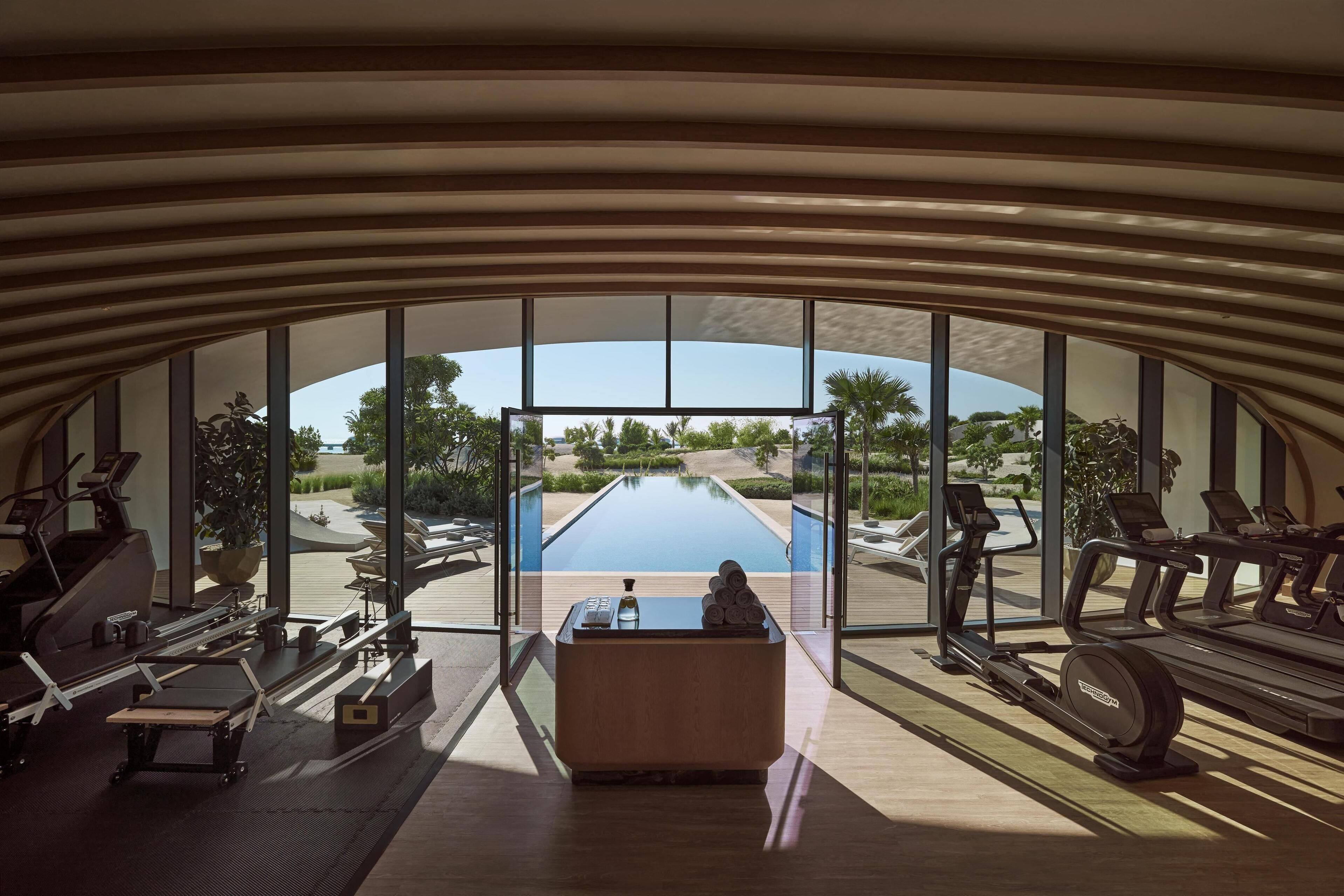 Et moderne fitnesscenter med stort vindue der giver udsigt over en pool og udendørs område.