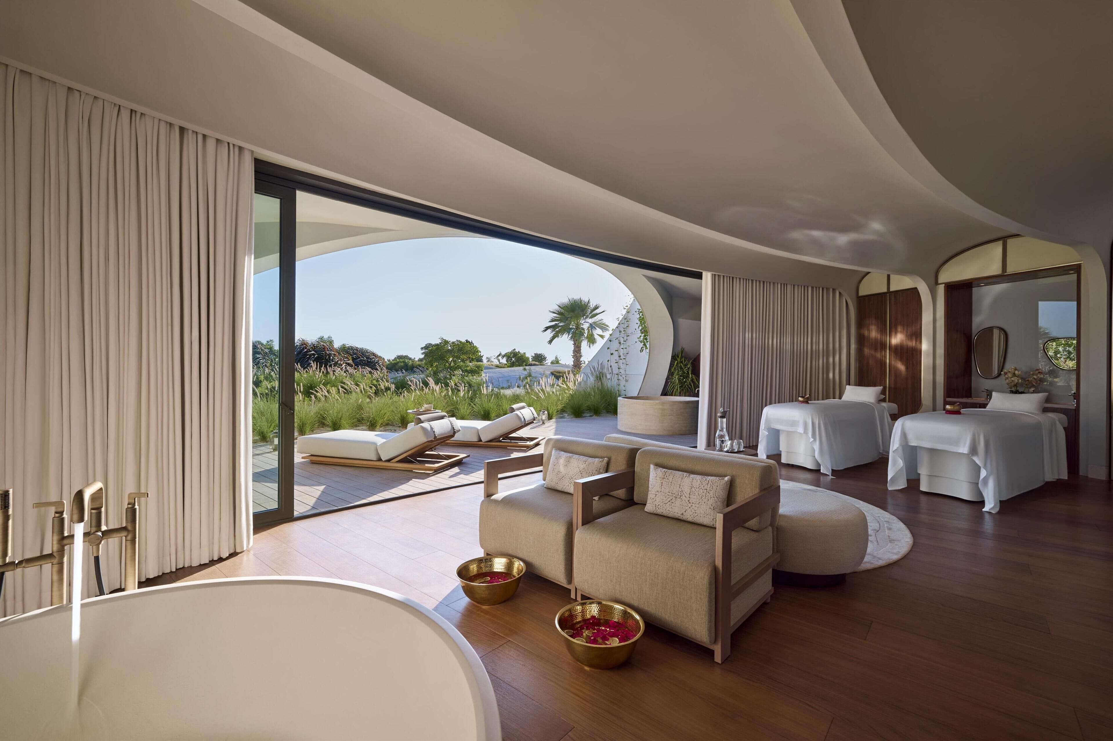 Un spa moderno con una bañera grande, dos sofás, una mesa de masaje y vistas al exterior.