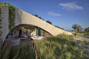 A modern building with a curved facade, outdoor seating area, and a view of the sea. - Shebara Resort (Umluj)
