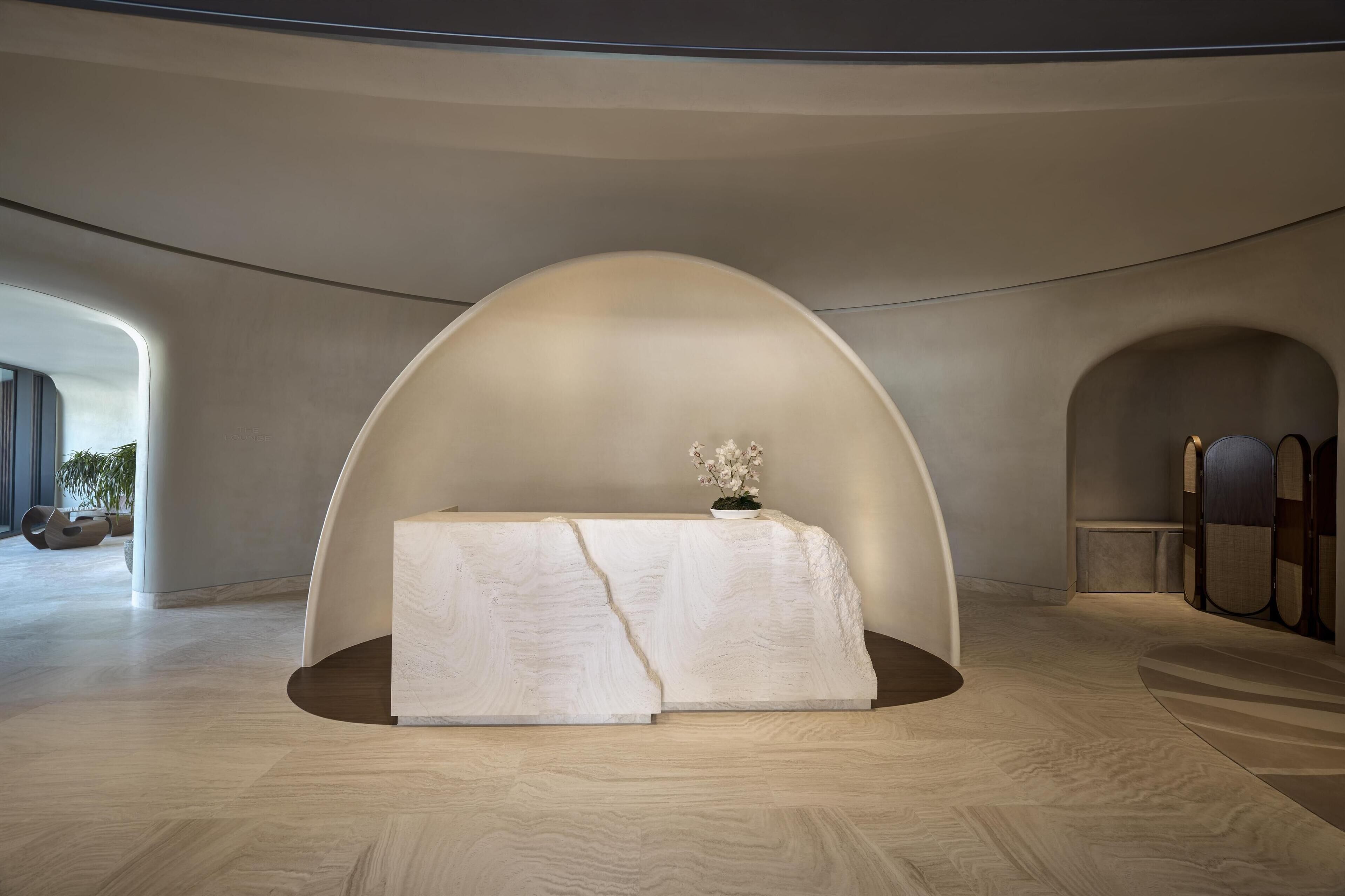 A modern interior with a central reception desk, arched ceiling, and wooden flooring.