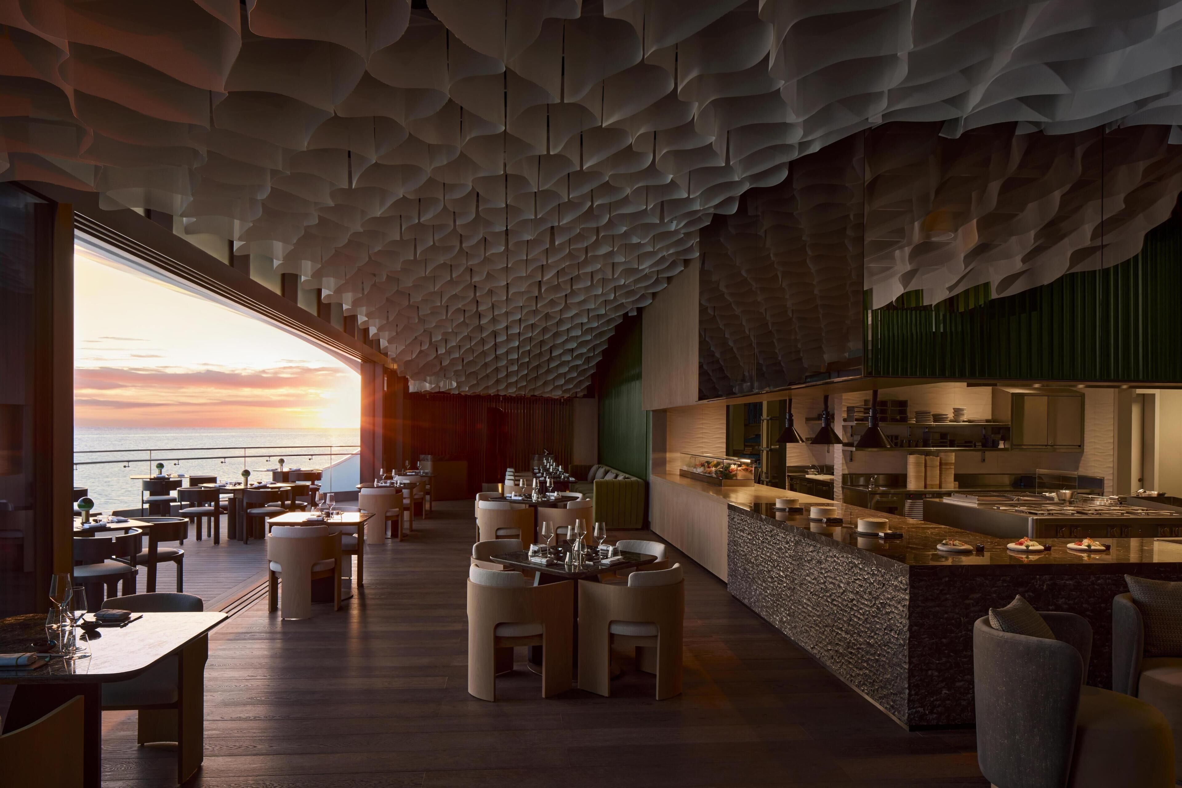 Ein modernes Restaurant mit einzigartigem Deckenstil, Blick auf den Sonnenuntergang und einer Bar.