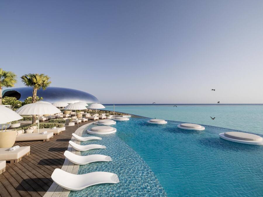 Zona junto a la piscina con sillas de descanso y sombrillas, cielo despejado y vista al océano.