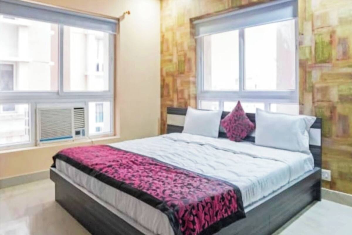 Un dormitorio con cama, dos ventanas, un radiador y una pared con diseño de piedra.