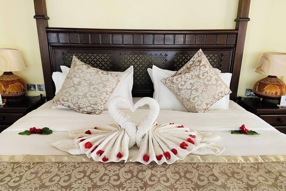 Uma cama bem arrumada com arranjo de toalhas em formato de coração e almofadas decorativas.