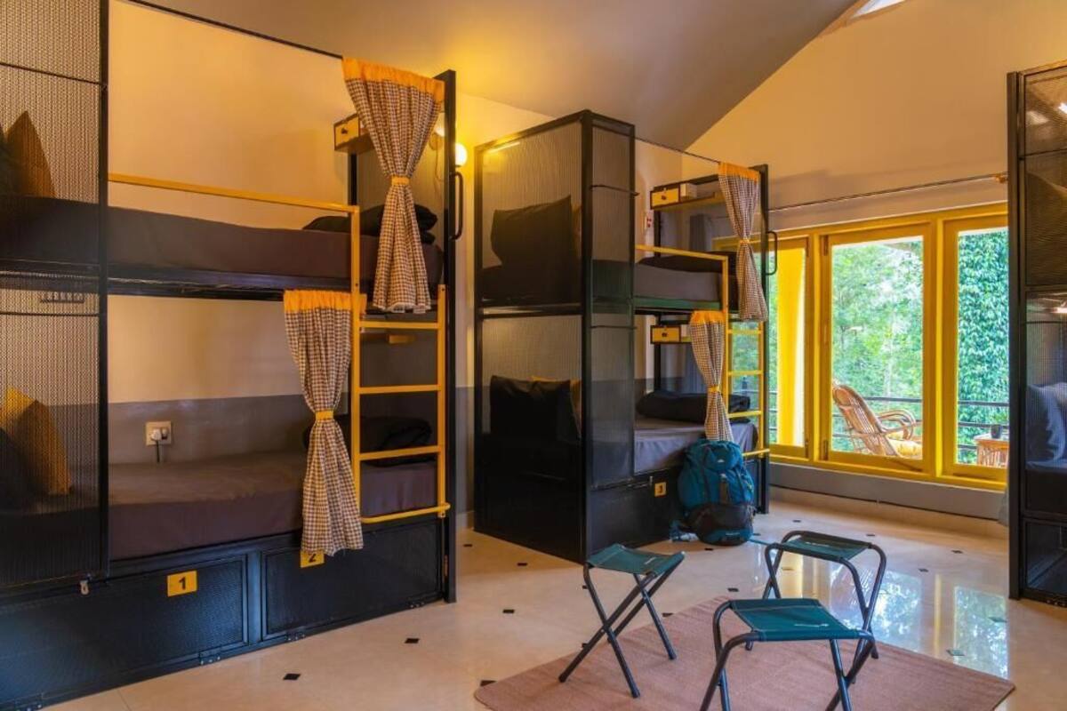 A compact room with bunk beds, a small seating area, and a large window offering a view of greenery.