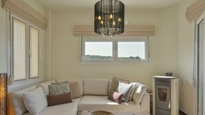 A modern living room with a beige sofa, a coffee table with decorative items, a built-in oven, and a large window with a view. - Mili Serenity (Rethymno)