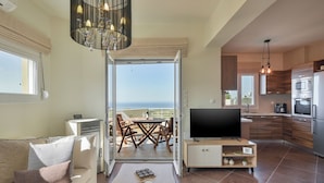 A modern living room with a sofa, TV, and dining area with a view of the sea. - Mili Serenity (Rethymno)