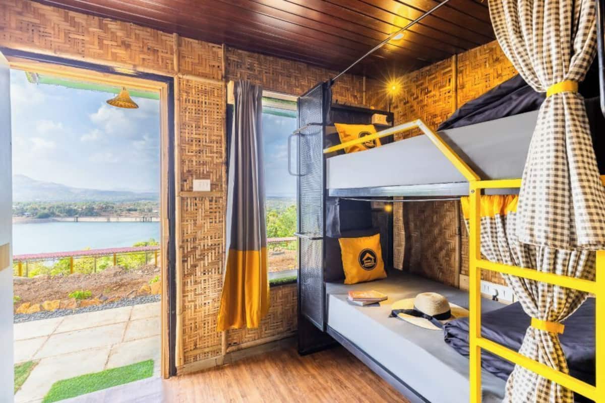 Dormitorio con literas y vistas a un lago y montañas, techo de madera y cortina a cuadros.