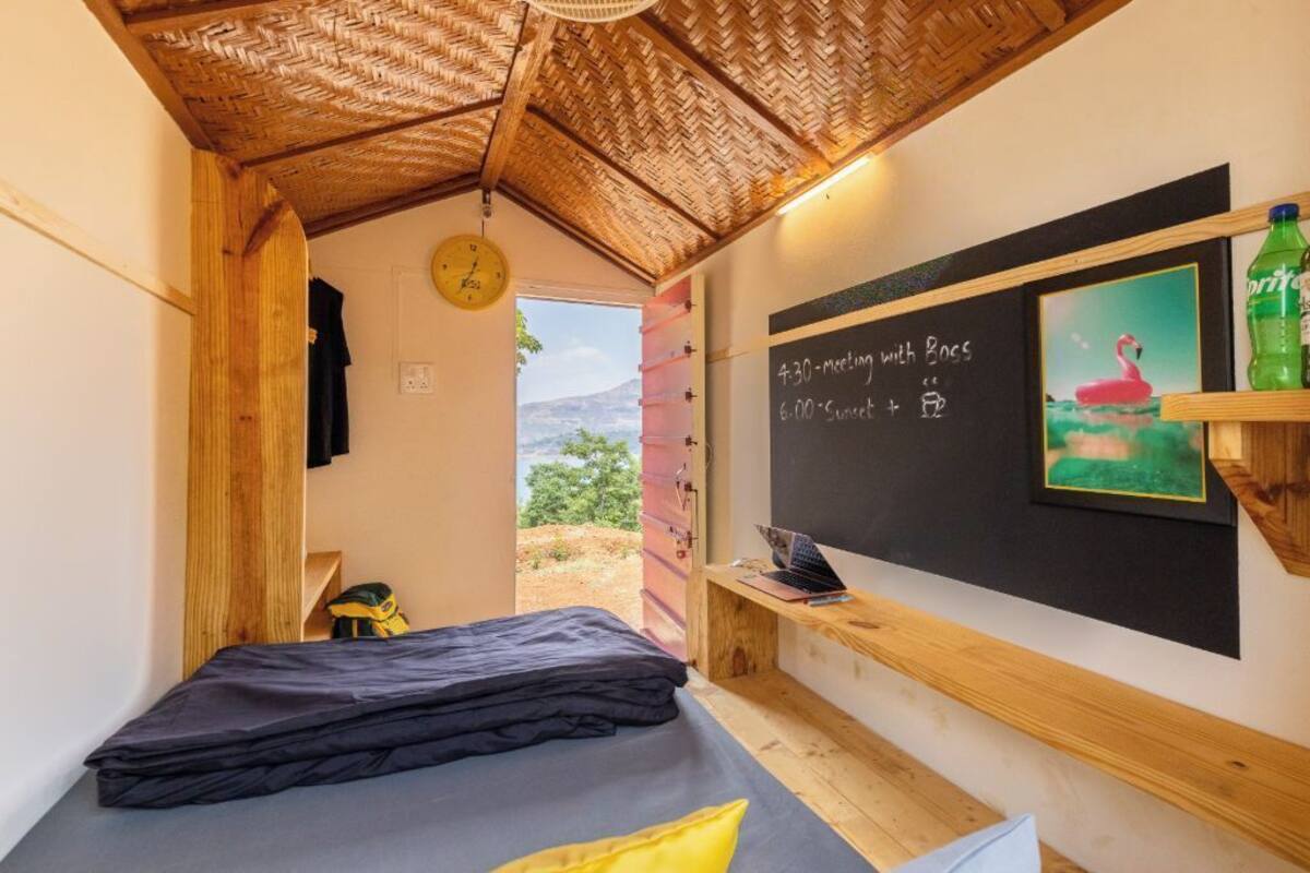 Una habitación con una cama, una pizarra con un horario, una computadora portátil, un reloj y vistas al exterior.