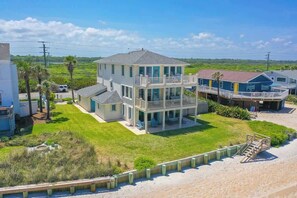 A large two-story house with a balcony, a small attached garage, and a beach view.