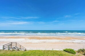 A beach with a wooden staircase leading down to the shore, a clear blue sky, and the ocean in the background. - High Tide Estate | Team Joseph Ellen (Ponte Vedra Beach)