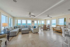 A spacious living room with a large sectional sofa, two accent chairs, a dining table, and a view of the ocean.