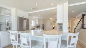 A spacious kitchen with white cabinetry, a central island with chairs, and a stainless steel refrigerator. - High Tide Estate | Team Joseph Ellen (Ponte Vedra Beach)