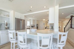 A spacious kitchen with white cabinetry, a central island with chairs, and a stainless steel refrigerator.