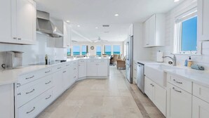 A spacious kitchen with white cabinetry, a central island, and a view of the ocean. - High Tide Estate | Team Joseph Ellen (Ponte Vedra Beach)